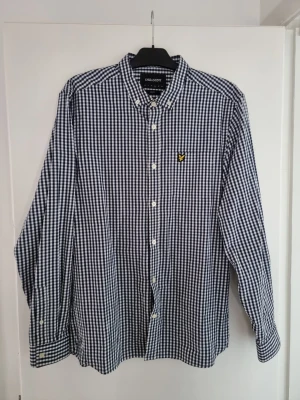 Blårutig skjorta från Lyle & Scott - Snygg blårutig skjorta från Lyle & Scott i slim fit-modell. Skjortan har klassisk button-down krage, vita knappar och det ikoniska gula logobroderiet på bröstet. Perfekt för dig som gillar stilrena och tidlösa plagg.