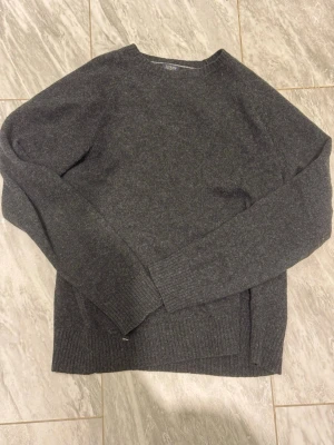 Mörkgrå stickad tröja J.Crew - Mysig mörkgrå stickad tröja från J.Crew med rund halsringning och ribbade muddar vid ärmslut och nederkant. Perfekt för lager på lager och enkel att matcha med olika stilar. Tillverkad i mjukt material som känns skönt mot huden.