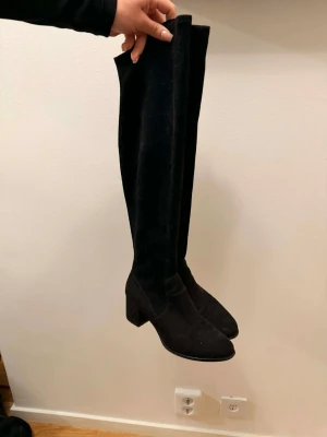 Svarta overknee stövlar med klack - Säljer ett par svarta overknee stövlar i mockaimitation med bred klack och rundad tå. Stövlarna har en stilren och trendig look som passar perfekt till höstens och vinterns outfits. De är höga! 