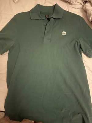 Grön pikétröja från G-Star RAW - Snygg grön pikétröja från G-Star RAW i storlek M. Klassisk modell med broderad logga på bröstet. I fint skick utan fläckar eller hål. Bekväm och passar både vardagligt och lite mer uppklätt. Öppen till bud 