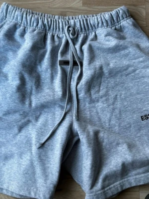 Grå shorts från Essentials - Snygga grå shorts från Essentials Fear of God med elastisk midja och snörning. Tillverkade i mjuk bomull för maximal komfort. Perfekta för chill dagar eller när du vill ha en avslappnad stil.