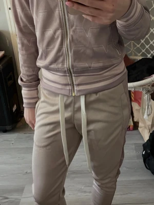 Beige mjukisbyxor  - Snygga beige mjukisbyxor med vita dragsnören Byxorna har ribbade muddar vid bensluten. Perfekta för en chill och sportig stil.