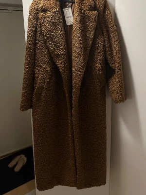 Brun lång teddyjacka från H&M - Supermysig lång teddyjacka i brun färg från nakd . Jackan har oversized passform, breda slag och är gjord i fluffigt teddy-material som håller dig varm. Perfekt för kalla dagar och ger en trendig look med sin långa siluett och mjuka känsla.