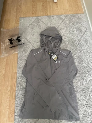 Under Armour vindjacka - lätt, bekväm och perfekt för både träning och vardagsbruk. Skyddar mot vind och passar bra med en sportig stil. I gott skick. Pris kan diskuteras vid snabb affär.