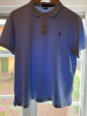 Ljusblå pikétröja från Ralph Lauren - Snygg ljusblå pikétröja från Polo Ralph Lauren i slim fit-modell. Klassisk krage, tre knappar och broderad logga på bröstet. Perfekt för dig som gillar stilrena och tidlösa plagg. Materialet är mjukt och skönt, passar till många olika outfits.