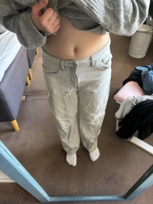 Ljusgrå raka jeans - Säljer ett par ljusgrå jeans med rak passform och klassisk femficksdesign. Jeansen har normal midja och stängs med dragkedja och knapp. Perfekta för en avslappnad och trendig look.