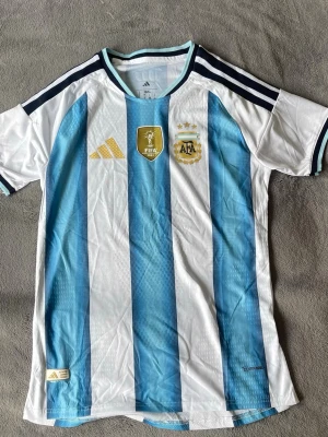 Argentina VM-vinnare 2022  - Sjukt clean Argentina-tröja med VM Champions badge och klassiska blåvita ränder 🔥 Minimalistisk men sticker ändå ut galet mycket.  • Argentina landslag • storlek M (L passar som M) • FIFA World Champions 2022 badge 🏆 • Climacool • Snygga detaljer och premiumkänsla i tyget • Perfekt till både vardag och fotboll  En riktig måste-ha tröja om man gillar fotboll eller bara vill ha en clean outfit 👌  💰 Pris: 400 kr 📍 Kan mötas / skickas  