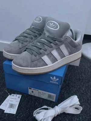 Adidas Campus 00S Grey - Plagg:Adidas Campus 00s Storlek:41 1/3 Nypris:1399 Mitt pris:399 Skick:9/10 Märke/Brand:Adidas Färg:Grå/Vit Material:Mocka Passform:41-42 även 43 Stora i Storleken Användning:Sparsamt använda Övrigt:  Kvitto finns på Mail, Kan maila de vid köp😃  Priset är inte hugget i sten🪨🪓 Fraktar Inom 24 h📦 Skriv Vid Minsta Lilla Intresse😃