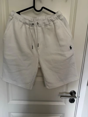 Vita shorts från Polo Ralph Lauren - Snygga vita shorts från Polo Ralph Lauren med klassisk broderad logga på benet. Shortsen har dragsko i midjan och sidofickor. Tillverkade i mjuk bomull för en bekväm känsla. Perfekta för sommardagar och avslappnade tillfällen.