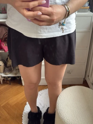 Svarta shorts med snörning och vågig kant - Säljer ett par svarta shorts med snygg snörning framtill och unik vågig kant nertill. Shortsen har en loose passform och är perfekta för sommaren. Tillverkade i ett mjukt material som känns skönt mot huden.