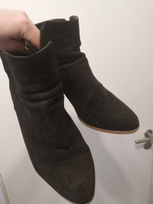 Svarta stövletter med klack - Svarta stövletter i mockaimitation med rundad tå och dragkedja på sidan. Skorna har en stadig klack i trälook och en stilren design som passar till många outfits. Perfekta för dig som gillar en klassisk och enkel stil.