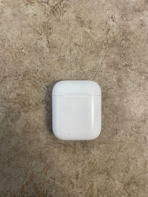 Apple AirPods med laddningsetui - Säljer ett par Apple AirPods med vitt laddningsetui. Etuiet är kompakt, har rundade kanter och är gjort i blank plast. Perfekt för trådlös musik och samtal, smidig att ta med överallt och enkel att använda med Apple-enheter.