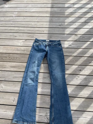 Blå bootcut jeans med utsvängda ben - Snygga blå bootcut jeans med klassisk femficksdesign och utsvängda ben. Jeansen har låg midja och är tillverkade i denim med lätt tvättad look. Perfekta för dig som gillar retrostil och vill ha ett par jeans som sticker ut.