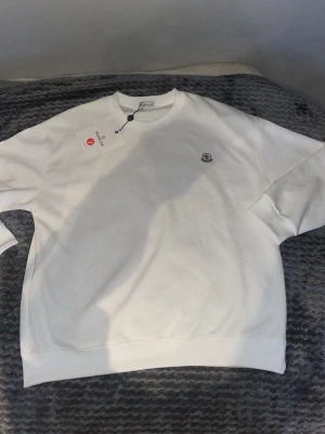 Vit sweatshirt från Moncler - Är L fast känns som M.Snygg vit sweatshirt från Moncler med rund halsringning och diskret Moncler-logga på bröstet. Tröjan har en klassisk passform och är tillverkad i mjukt material som känns skönt mot huden. Perfekt för en clean och stilren look.
