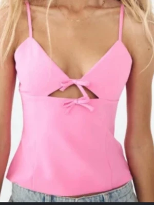 Rosa linnetopp med rosetter - liten i storlek så passar xs/s också!!! Snygg rosa linnetopp med smala axelband och två söta rosetter framtill. Toppen har en liten cut-out detalj under bysten och är figurnära i modellen. Perfekt att matcha med jeans eller kjol för en trendig look.