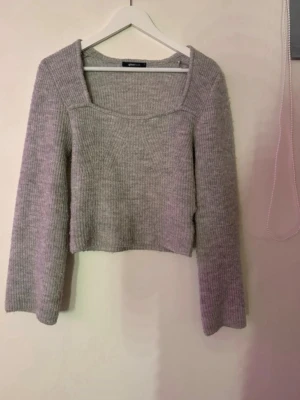 Grå stickad tröja Gina Tricot - Superfin grå stickad tröja från Gina Tricot med fyrkantig halsringning och långa ärmar. Tröjan är ribbstickad och har en något kortare, boxig passform. Perfekt att styla med jeans eller kjol för en trendig look.