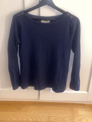 Marinblå långärmad tröja Hampton Republic - Mörkblå långärmad tröja från Hampton Republic med rund halsringning och dekorativa knappar på axlarna. Broderad logga på ärmen. Perfekt för en stilren och avslappnad look.