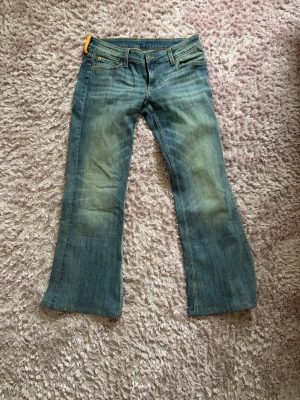 Blå bootcut jeans med slitningar - Snygga blå bootcut jeans med lätt slitna detaljer framtill och klassiska bakfickor. Jeansen har låg midja och är tillverkade i denim med en skön känsla. Perfekta för dig som gillar en avslappnad och trendig stil. Uppsydda för att passa 165, men aldrig använda!