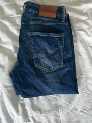 Mörkblå jeans från Jack & Jones - Snygga mörkblå jeans från Jack & Jones med klassisk femficksdesign och kontrastsömmar. Jeansen har en läderpatch med logga bak i midjan och lätt slitna detaljer framtill för en cool look. Perfekta till vardagsstilen.