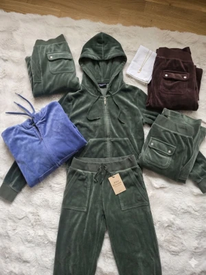 Grön, blå, brun velour loungewear-set Juicy Couture - Säljer en samling av mina Juicy Couture velour-favoriter! Alla delar är sparsamt använda. De är otroligt mjuka och har den perfekta passformen. Vad som finns: Mörkgrönt Set (S): Full-zip hoodie med och matchande byxor. (1200 kr för setet). Chokladbruna Byxor (XS): Med fickor bak och krispiga detaljer. (650kr) Lila Hoodie (XS): Full-zip med fin lyster. (550kr) Extra Mörkgröna Byxor (XS): Perfekt passform.  Kan säljas som ett komplett set eller som enskilda delar.Kom gärna med bud vid snabb affär.