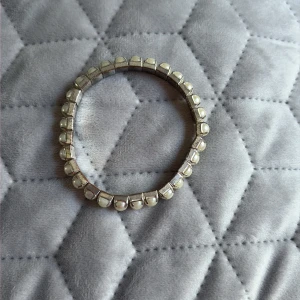 Elastiskt armband med vita pärlor - Snyggt armband med vita pärlor på elastiskt band. Pärlorna är runda och sitter tätt intill varandra runt hela armbandet. Perfekt accessoar för att ge din outfit en elegant touch. Metallfärgad bas mellan pärlorna.