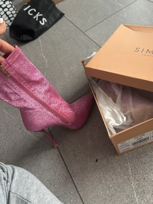 Glittriga rosa stövletter från Simmi - Säljer ett par glittriga rosa stövletter från Simmi London. De har spetsig tå, smal stilettklack och dragkedja på sidan. Skorna är täckta av glittermaterial som verkligen sticker ut. Perfekta för dig som vill ha något extra till outfiten.
