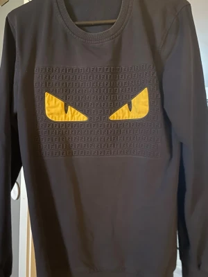 Fendi sweatshirt   - Cool svart sweatshirt från Fendi med ikoniska gula monsterögon och diskret Fendi-mönster på bröstet. Tröjan har rund halsringning och långa ärmar. Perfekt för dig som vill sticka ut med en unik designertröja.