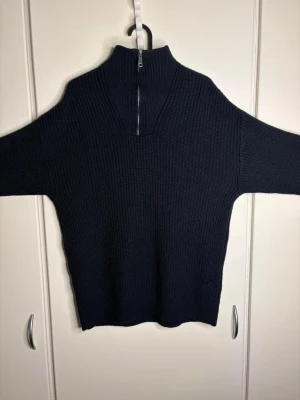 Mörkblå stickad tröja med halvzip - Mörkblå stickad tröja med hög krage och halvzip framtill. Tröjan har lång ärm och är ribbstickad för en skön och avslappnad look. Perfekt för lager på lager och passar till både jeans och kjol. SITTER LITE STÖRRE ÄN XS SKULLE SÄGA MER ÄN S ELLER M