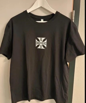 Svart West Coast Choppers t-shirt - Svart t-shirt från West Coast Choppers med klassiskt kors-tryck och logga på både bröstet och ryggen. T-shirten har rund hals och normal passform. Perfekt för dig som gillar streetwear och motorcykelkultur. 3xl men passar 2xl 