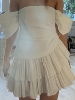Studenklänning Vit offshoulder klänning med volang - Superfin vit klänning med offshoulder-design och kort längd. Klänningen har två lager plisserade volanger som ger en snygg och lekfull look. Perfekt för dig som vill sticka ut och känna dig extra stylish. Materialet känns lätt och bekvämt. Köpt för 1500 från ASOS med prislapp kvar men han inte rerunera 