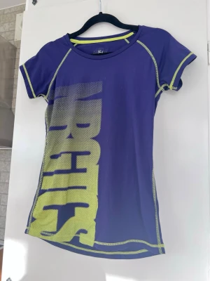 Lila tränings-tshirt, stl S - En lila tränings-t-shirt, förmodligen inköpt på Stadium/Intersport eller liknande.  Är från barnavdelningen (flicka) i stl 150, men passar bra till mig som normalt är storlek S.  Använd en hel del men fortfarande i bra skick (se bilder).