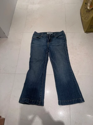 Blå lågmidjade bootcut jeans  - Ett par klassiska blå bootcut jeans från Faded Glory med snygga kontrastsömmar. Jeansen har låg midja och utsvängda ben, perfekt för en avslappnad och trendig look. Tillverkade i slitstark denim. 90cm längd från topp till tå och 40cm i midjan när byxorna är utlagda från sida till sida. 