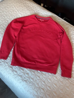 Röd sweatshirt från Race Marine - Snygg röd sweatshirt från Race Marine med broderad text på bröstet. Tröjan har rund halsringning, långa ärmar och ribbade muddar vid ärmslut och nederkant. Perfekt för en avslappnad och sportig stil. Storlek S