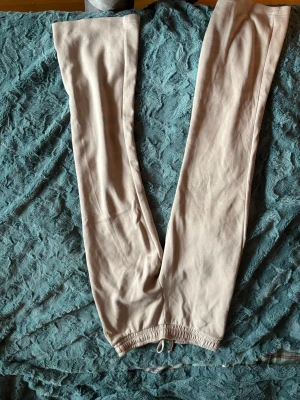 Beige mjukisbyxor med dragsko - Säljer ett par beige mjukisbyxor med resår och dragsko i midjan. Byxorna har raka ben och är gjorda i ett mjukt och bekvämt material, perfekta för chill dagar hemma eller när du vill ha det extra comfy.