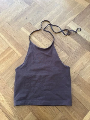 Brun halterneck linnetopp - Säljer en brun halterneck linnetopp med knyt i nacken. Toppen har en enkel och stilren design med rak nederkant och ärmlös modell. Perfekt för att skapa en trendig look till sommaren.
