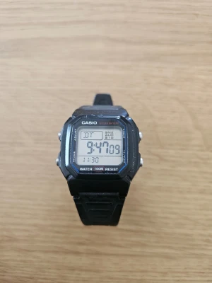 Svart digital klocka från Casio - Klassisk digital klocka från Casio i svart med fyrkantig display och gummiband. Klockan har flera funktioner som alarm, datumvisning och är vattentålig upp till 100 meter. Perfekt för dig som gillar enkel och tidlös stil.