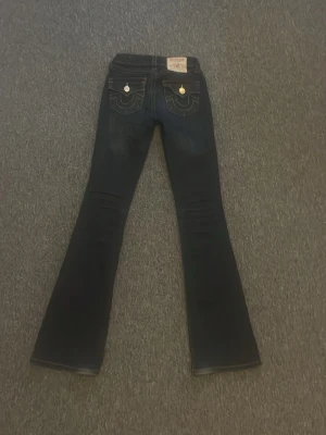 Mörkblå bootcut jeans från True Religion -  Säljer för 800, nypris är 1300.Säljer ett par mörkblå bootcut jeans från True Religion med snygga kontrastsömmar och dekorativa fickor bak med guldfärgade knappar. Jeansen har klassisk femficksdesign och är tillverkade i denim.