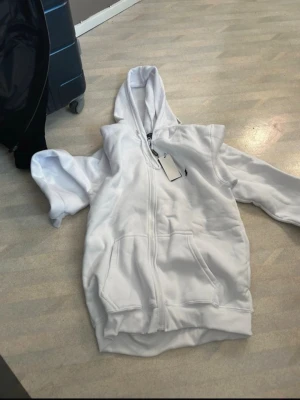 Vit hoodie med dragkedja från Polo Ralph Lauren - Säljer en fräsch vit hoodie från Polo Ralph Lauren med dragkedja framtill och klassisk huva. Hoodien har två stora fickor fram och den ikoniska lilla loggan på bröstet. Perfekt för en clean och stilren look.