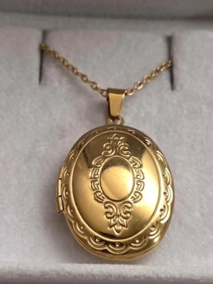 Guldfärgat ovalt medaljonghalsband - Snyggt guldfärgat halsband med oval medaljong som har fina graverade detaljer på framsidan. Medaljongen går att öppna för att lägga in ett foto eller minne. Kedjan är tunn i rostfritt stål och matchar medaljongens eleganta look. Perfekt accessoar för dig som gillar klassisk stil.