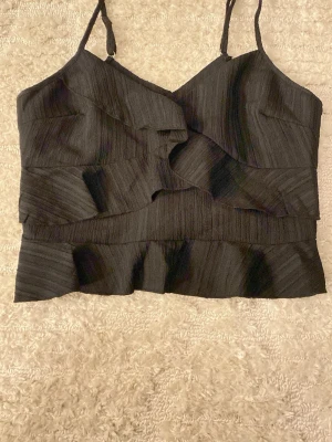 Svart volang topp med smala axelband - Säljer denna svarta topp med smala axelband och volangdetaljer framtill och nedtill. ❤️ Jag säljer denna då jag inte var nöjd på grund av att den inte passade mig, den passar xs men mer åt storleken s. Toppen är från shein ❤️