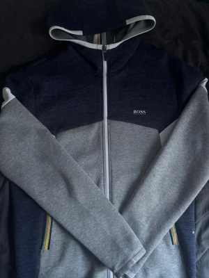 Grå och marinblå hoodie från BOSS - Blå och grå zip up hoodie från boss, inga defekter alls. Storleken är M och passar M, kom dm för fler bilder och om ni har frågor.