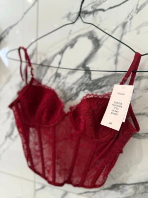 Vinröd spetsbody från H&M - Snygg vinröd body från H&M i spets med vadderade kupor och justerbara axelband. Transparent material med fina spetsdetaljer och markerade sömmar framtill. Helt ny, med prislapp