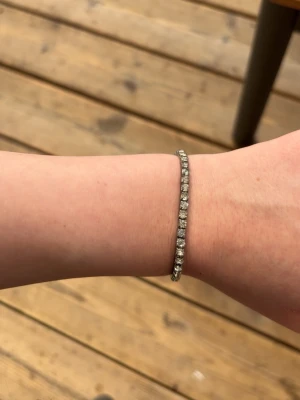 Silverfärgat armband med pärlor - Ett stilrent armband i silverfärg med glittrande pärlor längs hela bandet. Armbandet är smalt och har en klassisk design som passar perfekt för dig som gillar enkel men elegant stil. Perfekt att kombinera med andra smycken för en personlig look.