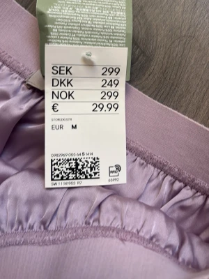 Ljuslila plisserad kjol i satin - Superfin ljuslila plisserad kjol i satinliknande material. Kjolen har resår i midjan och ett snyggt fall som ger en flowig känsla. Perfekt för dig som vill ha en trendig och bekväm kjol med lite extra glans.