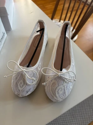 Vita spetsballerinaskor med rosett - Snygga vita ballerinaskor från Super Mode med spetsdetaljer och dekorativ rosett framtill. Aldrig använda. 