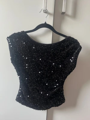Svart paljettopp med öppen rygg - Snygg svart topp täckt med glittrande paljetter och en djup öppen rygg. Modellen är ärmlös och har en figurnära passform som ger en riktigt festlig look. Perfekt för dig som vill sticka ut och glänsa. Storlek M men passar bra på mig som vanligtvis har S/Xs💕