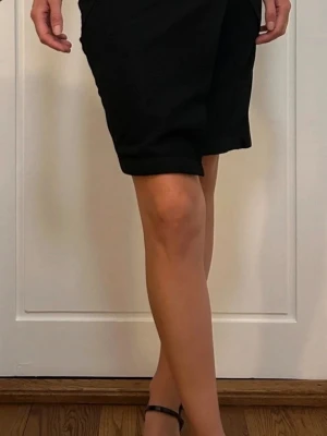 Svart kortkjol med asymmetrisk design - Svart kortkjol med snygga asymmetriska sömmar och stilren look. Kjolen har en rak passform och är tillverkad i ett mjukt material som känns bekvämt. 