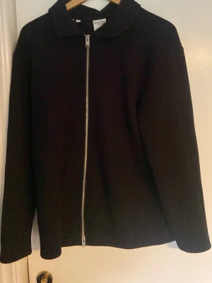 Svart jacka med dragkedja från Selected - Stilren svart jacka från Selected med hel dragkedja framtill och klassisk krage. Jackan har en rak passform och är tillverkad i ett mjukt tyg som ger en clean look. Perfekt för dig som gillar minimalistisk stil.