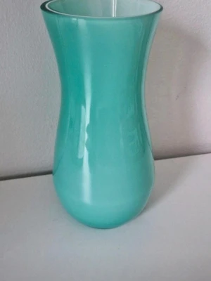 Turkos glasvas med modern form - Snygg turkos vas i glas med mjukt böjd siluett och blank yta. Perfekt som inredningsdetalj eller för blommor. Stilren design som passar i de flesta rum och ger en fräsch färgklick till hemmet.