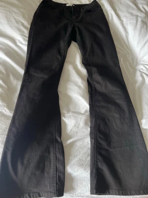 Svarta bootcut jeans - Snygga svarta jeans med utsvängda ben. Jeansen har hällor för skärp och är tillverkade i ett denimtyg. Perfekta för dig som gillar en trendig och bekväm stil.